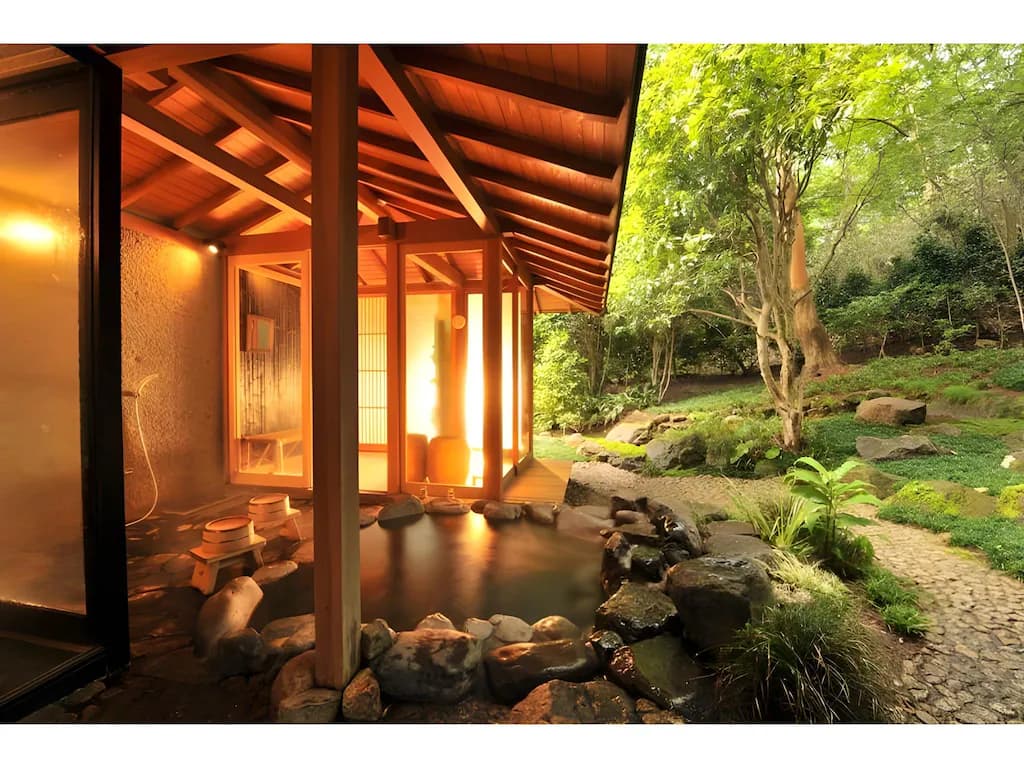 Private open-air stone onsen at Gora Kadan ryokan, illuminated by warm golden light and surrounded by a lush moss-covered Japanese garden.