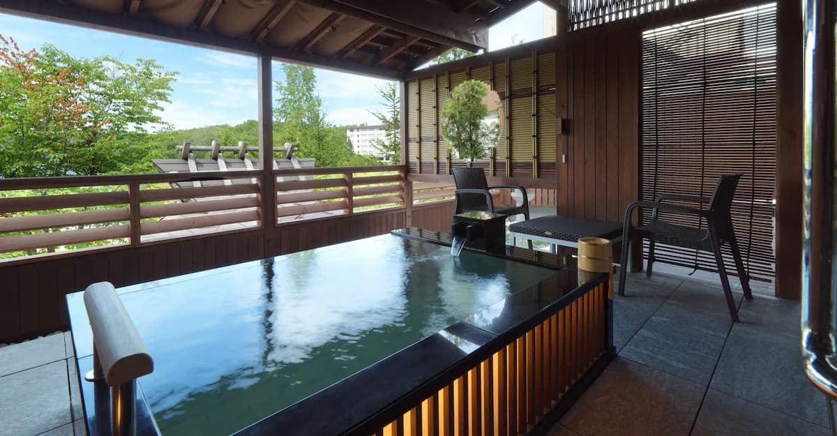 Private open-air hot spring bath with clear reflective water on a wooden terrace, offering views of lush green forests and Lake Akan at Akan Tsuruga Bessou Hina no Za.